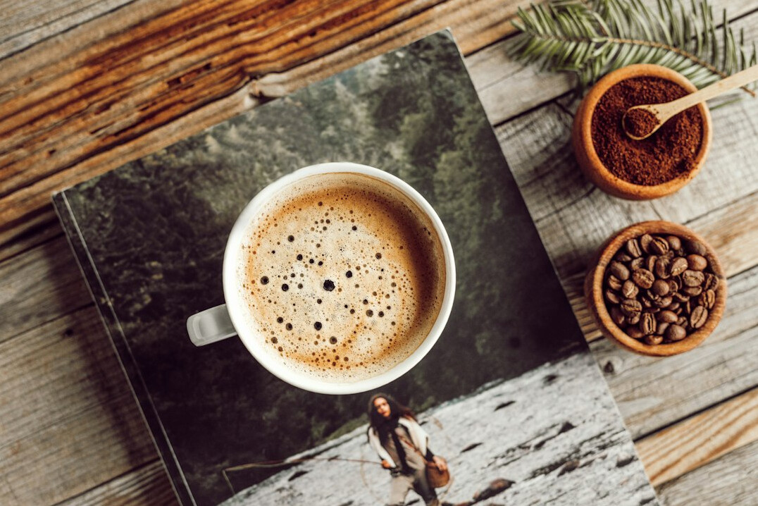 Cup of coffee, open notebook and calculator on a wooden table in morning light